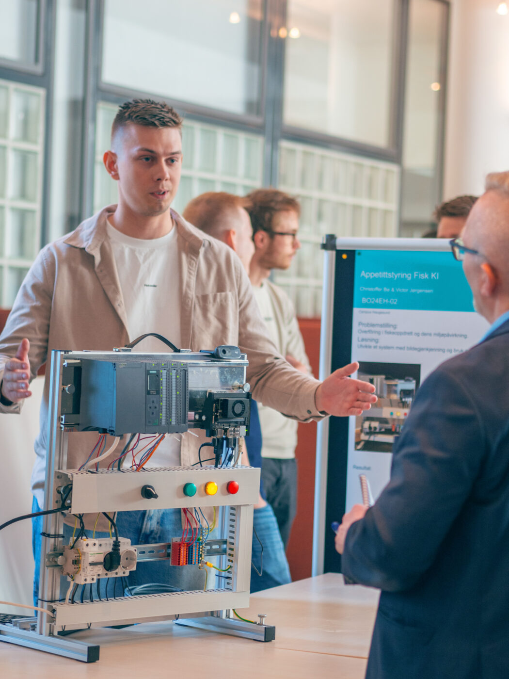 To menn snakker sammen på en stand med et elektronisk apparat mellom seg.