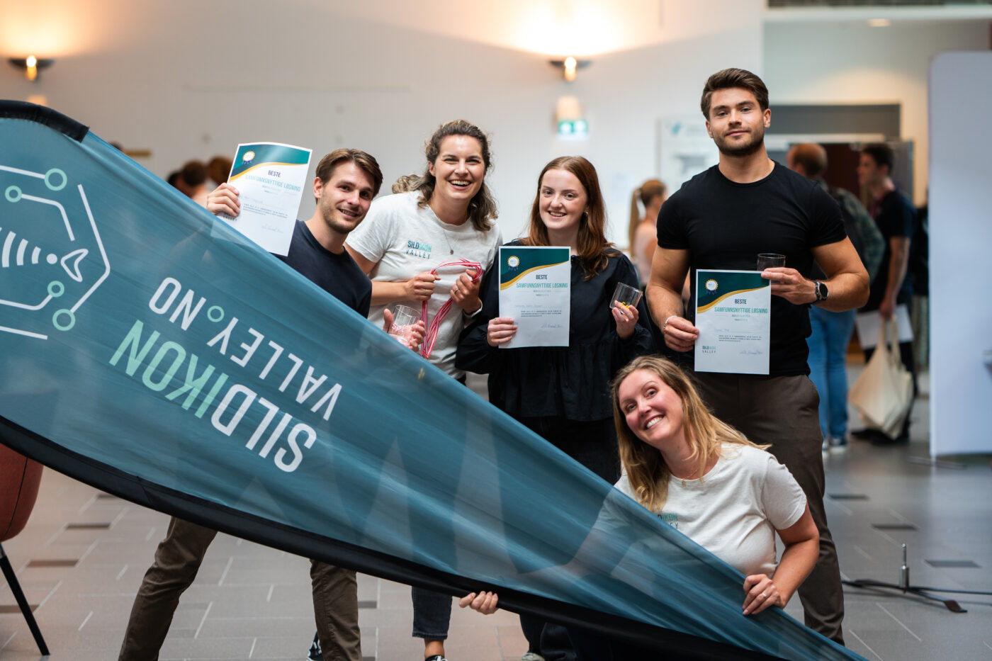 Tre smilende studenter og to ansatte i Haugaland Vekst bak et Sildikon Valley-banner. Studentene holder premier og diplomer merket "Beste samfunnsnyttige løsning".