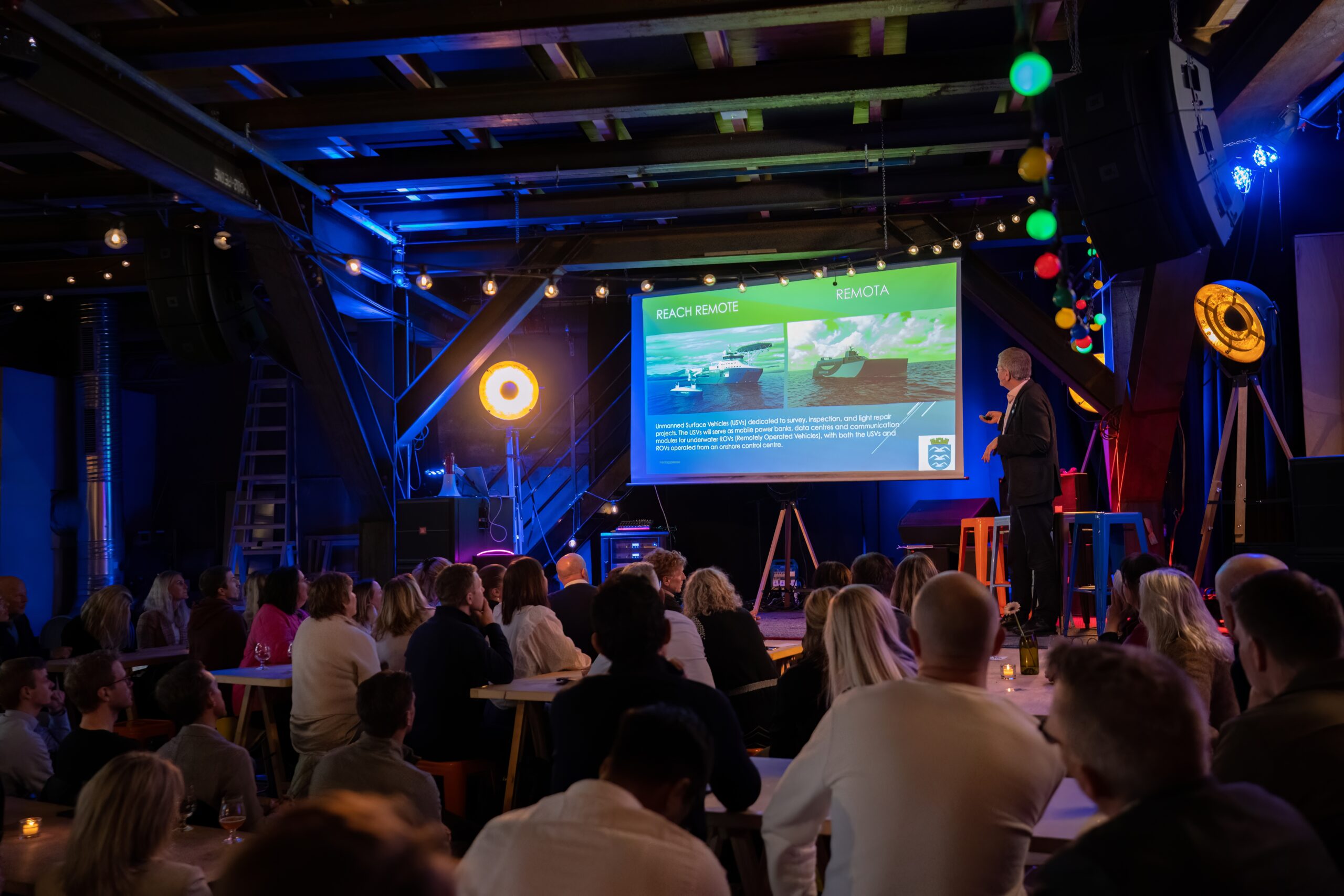 Seminar på Grunderloftet. Presentasjon med powerpoint på scenen og mange folk i salen.